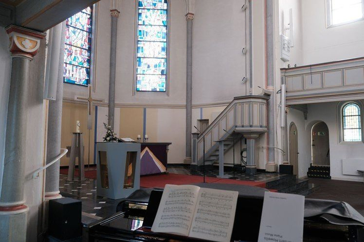Erhöhte Ansicht des Kircheninneren mit Altar, Kanzel, Klavier und Empore.