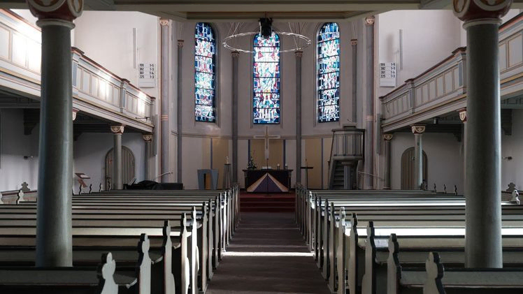 Kircheninneres mit Bänken, Buntglasfenstern, Altar und Empore.