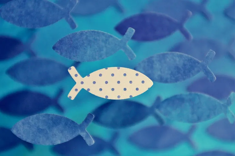 Gepunkteter Fisch schwimmt gegen einen Schwarm einfarbig blauer Fische.