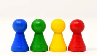 Vier bunte hölzerne Spielfiguren (blau, grün, gelb, rot) in einer Reihe.