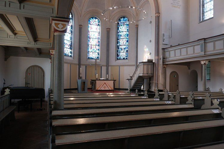 Kircheninneres mit Bänken, Altar, Kanzel und Buntglasfenstern.