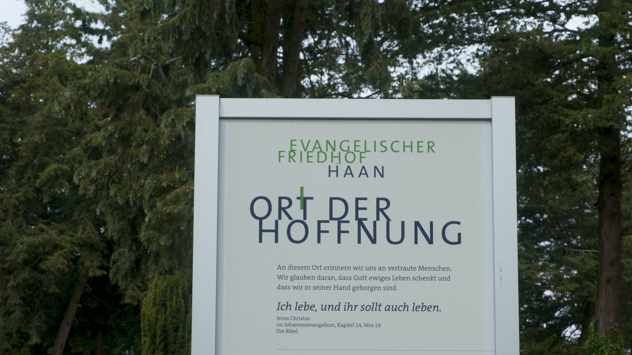 Schild für "Evangelischer Friedhof Haan," ein Ort der Hoffnung, umgeben von Bäumen.