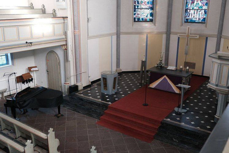 Erhöhte Ansicht des Kircheninneren mit Altar, Kanzel, Klavier und Empore.