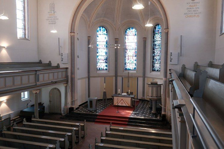 Kirchenraum mit Bänken, Altar, Kanzel, Buntglas und Empore.