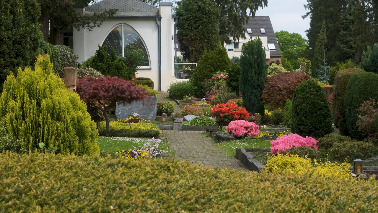 Üppiger Friedhofsgarten mit gewundenen Steinpfaden und vielfältigen Pflanzen.