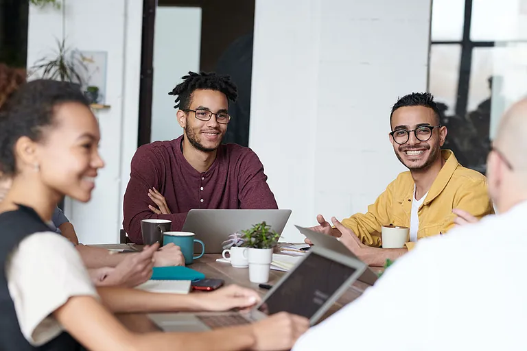Diverse Gruppe junger Berufstätiger arbeitet gemeinsam an einem Tisch mit Laptops.