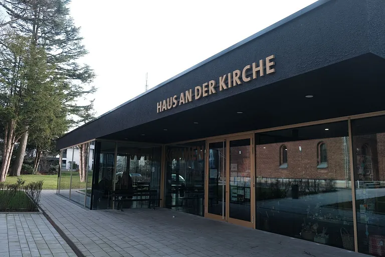 "Haus an der Kirche" Gebäude mit modernem Design und Glasfassade.