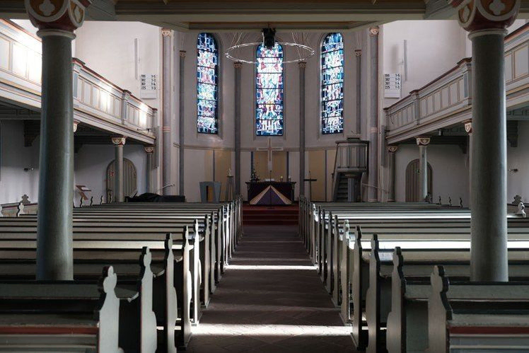 Kircheninneres mit Bänken, Buntglasfenstern, Altar und Empore.