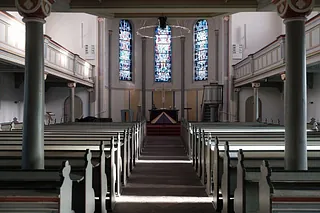 Leeres Kircheninterieur mit Bänken, Buntglasfenstern und erhöhter Kanzel.