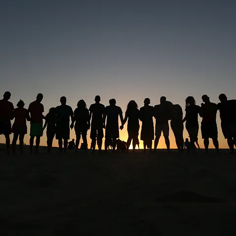 Silhouettierte Gruppe von Menschen steht an einem Strand bei Sonnenuntergang in Angeles.