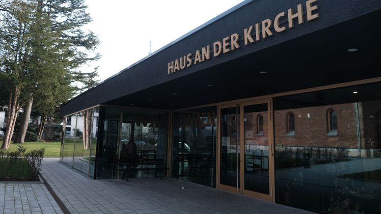Haus an der Kirche" Gebäude mit modernem Design und gläsernem Eingang.