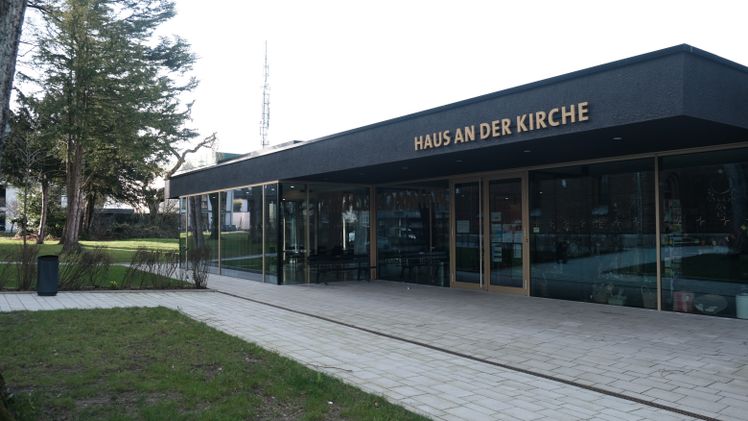 Außenansicht des "Haus an der Kirche" mit Glasfassade und Gehweg.