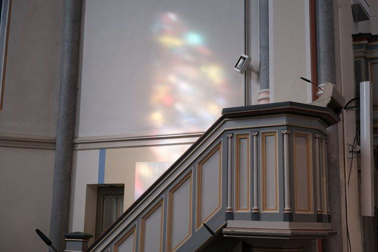 Kirchenkanzel mit Treppe, Mikrofon, und reflektiertem Buntglaslicht.